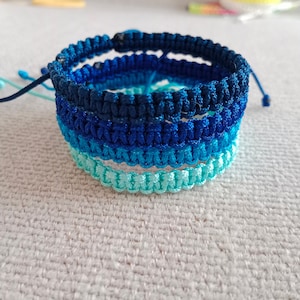 May include: A multi-layered bracelet made of blue and turquoise braided cords. The bracelet is tied with a knot at the end.