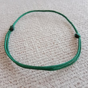 May include: A green cord necklace with black knots at the ends.