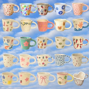 Könnte beinhalten: Eine Sammlung von Keramikbechern mit verschiedenen Designs, darunter Kirschen, Blumen und abstrakte Muster. Die Becher sind in verschiedenen Farben wie Rosa, Blau und Grün gehalten und haben einzigartige Griffformen.