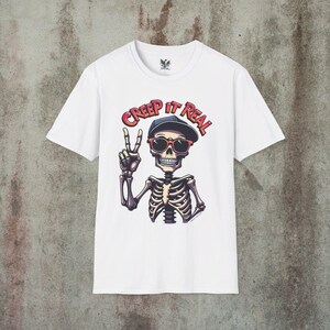 Creep It Real Skeleton T-Shirt featuring a cool illustration of a skeleton flashing the peace sign, wearing sunglasses and a hat, with the slogan Creep It Real on a black unisex t-shirt, perfect for Halloween partygoers and casual wear.
