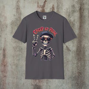 Creep It Real Skeleton T-Shirt featuring a cool illustration of a skeleton flashing the peace sign, wearing sunglasses and a hat, with the slogan Creep It Real on a ice grey unisex t-shirt, perfect for Halloween partygoers and casual wear.