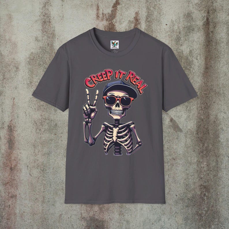 Creep It Real Skeleton T-Shirt featuring a cool illustration of a skeleton flashing the peace sign, wearing sunglasses and a hat, with the slogan Creep It Real on a ice grey unisex t-shirt, perfect for Halloween partygoers and casual wear.