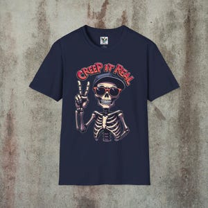 Creep It Real Skeleton T-Shirt featuring a cool illustration of a skeleton flashing the peace sign, wearing sunglasses and a hat, with the slogan Creep It Real on a navy blue unisex t-shirt, perfect for Halloween partygoers and casual wear.