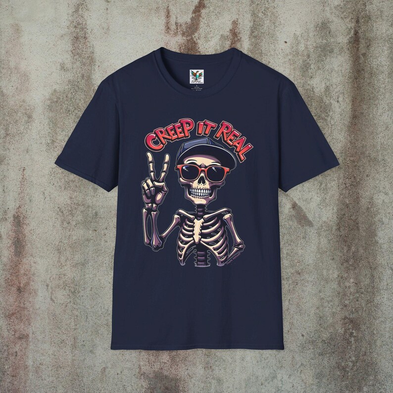 Creep It Real Skeleton T-Shirt featuring a cool illustration of a skeleton flashing the peace sign, wearing sunglasses and a hat, with the slogan Creep It Real on a navy blue unisex t-shirt, perfect for Halloween partygoers and casual wear.