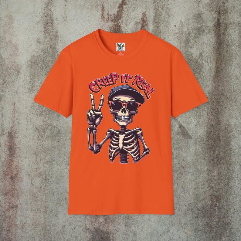 Creep It Real Skeleton T-Shirt featuring a cool illustration of a skeleton flashing the peace sign, wearing sunglasses and a hat, with the slogan Creep It Real on a charcoal unisex t-shirt, perfect for Halloween partygoers and casual wear.