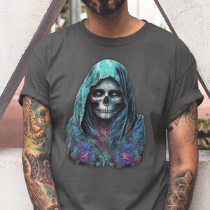 May include: A dark gray t-shirt with a graphic print of a hooded figure with a blue and green skull face. The skull has white eyes and a detailed design. The figure is surrounded by blue and purple flowers.