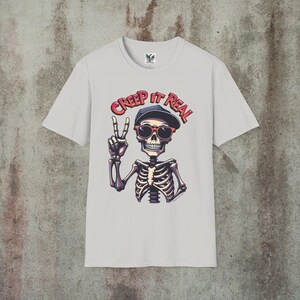 Creep It Real Skeleton T-Shirt featuring a cool illustration of a skeleton flashing the peace sign, wearing sunglasses and a hat, with the slogan Creep It Real on a white unisex t-shirt, perfect for Halloween partygoers and casual wear.