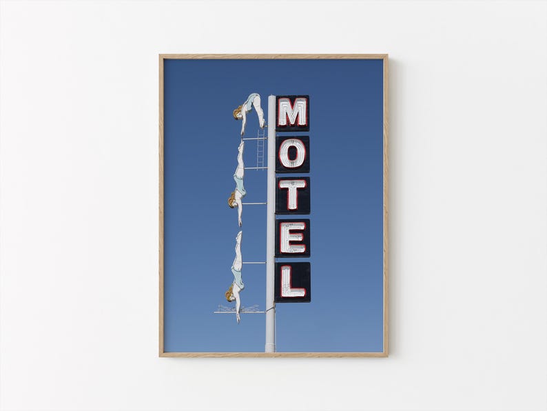 May include: A framed print featuring a blue sky background with a vintage motel sign. The sign spells out "MOTEL" in white letters with red outlines. Three figures in light blue swimsuits are diving from a ladder.
