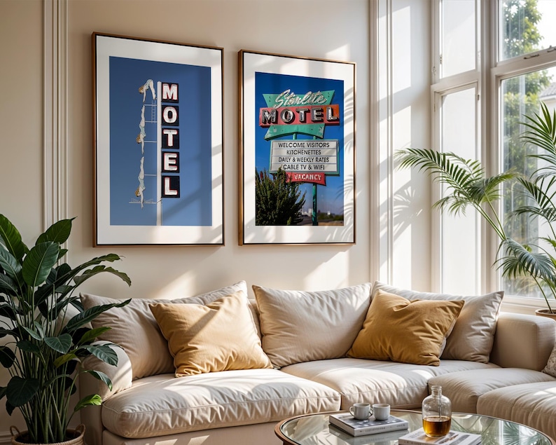 May include: Two framed prints of vintage motel signs hang above a beige sofa with gold pillows. One print shows a blue sky with the word "MOTEL" in neon lights. The other print displays a sign that reads "Starlite MOTEL" with additional text.