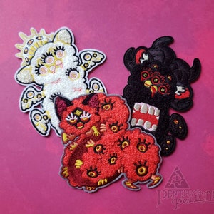以下が含まれることがあります： 奇抜なモンスターデザインの刺繍パッチ3枚。パッチは白、赤、黒で、それぞれ複数の目と独特の特徴があります。パッチはピンク色の背景にあります。「Identity Pollution」の文字が右下にあります。