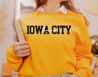 May include: A yellow sweatshirt with the text "IOWA CITY" in black letters. The word "Iowa" is written in white cursive script.