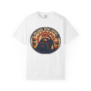 May include: A white t-shirt featuring a circular graphic of a raccoon in a hoodie working on a laptop. The design includes stacks of coffee mugs, a lit candle, a gear background, and the text ROLLBACK. RETRY. REPENT. in a bold yellow font.