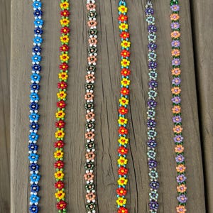 May include: Six beaded bracelets with floral designs. Each bracelet features a different color scheme, including blue, red, yellow, green, purple, and orange. The bracelets are made of small beads and have silver clasps.