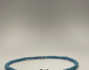 Puede incluir: Un brazalete de cuentas azul claro con una sola cuenta negra y blanca en el centro.