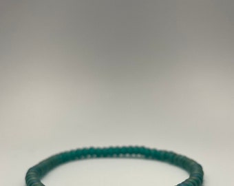 Puede incluir: Un brazalete de cuentas azul turquesa con dos cuentas en forma de estrella y una cuenta de vidrio azul en el centro.