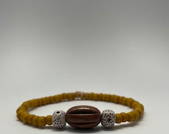 Puede incluir: Un brazalete de cuentas de color amarillo mostaza con dos cuentas blancas y una cuenta de madera marrón en el centro.