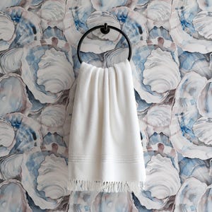 May include: A white towel with fringe hangs from a black metal towel ring. The towel is against a wall with a blue and white oyster shell pattern.