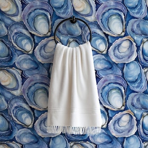 May include: A white towel with fringe hangs from a black metal ring against a blue and white oyster shell patterned wallpaper. The towel has a textured appearance and a decorative border.