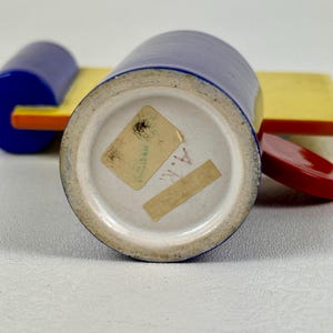 May include: A blue ceramic jar with a white bottom and a yellow and orange lid. The jar has a sticker on the bottom that says "A.K."