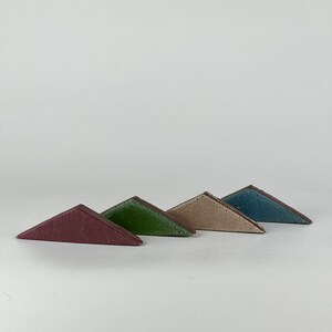 May include: Four ceramic triangle tiles in different colors: burgundy, green, beige, and blue. The tiles are arranged in a staggered pattern, with the burgundy tile at the bottom and the blue tile at the top.