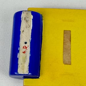 May include: A blue and yellow ceramic tile with a white stripe and red markings. The tile has a rectangular shape with a cutout in the center.