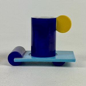 May include: A blue and yellow ceramic espresso cup and saucer set. The cup has a unique handle shaped like a yellow circle. The saucer is light blue with a blue rim.