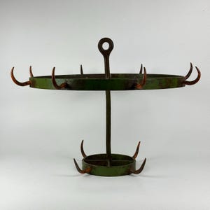 May include: A green metal stand with multiple hooks for hanging items. The stand has a round top and a round base with a decorative design.