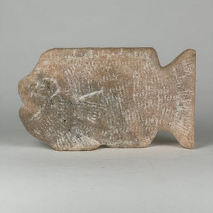 May include: A carved stone fish sculpture with a light brown color and a rough, textured surface.