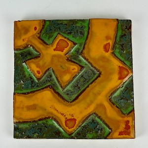 May include: A square ceramic tile with an abstract design. The tile features a yellow and green geometric pattern with orange accents.