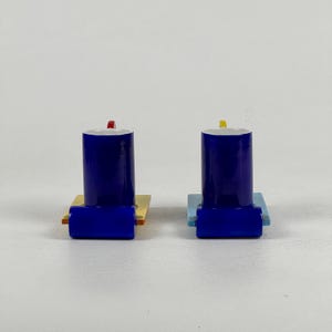 May include: Two blue ceramic cups with yellow, red, and blue square bases. The cups are upside down.