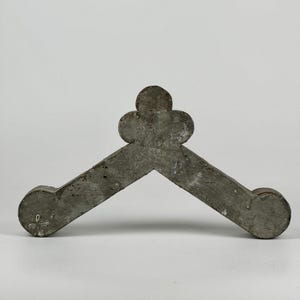 May include: A gray, wooden, decorative architectural element shaped like a V with a four-leaf clover design at the top.