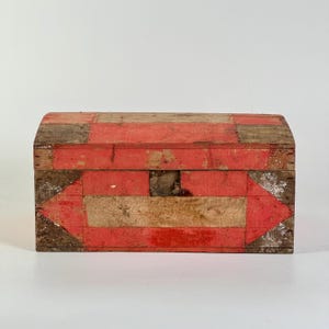 May include: A small, antique wooden chest with a curved top. The chest is painted with red and natural wood stripes and features a metal latch. The chest is likely used for storage and adds a rustic touch to any space.