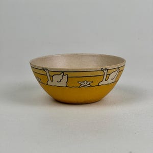 May include: A yellow ceramic bowl with a white rim and a black and white design of swans on a yellow background.