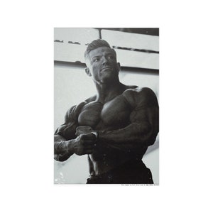 May include: Black and white photograph of a muscular man with a short haircut, posing with his arms crossed in front of him.