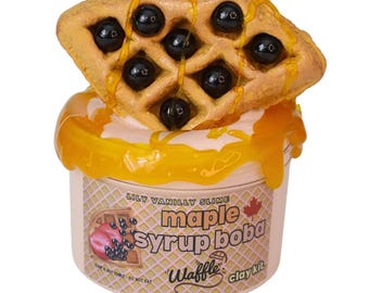 May include: A novelty slime kit featuring a waffle with dark boba pearls and maple syrup. The container is labeled "Lily Vanilly Slime" and "maple syrup boba waffle clay kit". The slime is pink and the syrup is a golden color.