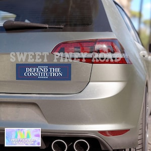 Puede incluir: Un coche plateado con una pegatina de parachoques azul y blanca que dice "DEFEND THE CONSTITUTION" con estrellas arriba y abajo del texto. La pegatina est&aacute; en la parte trasera del coche, debajo de los faros traseros.