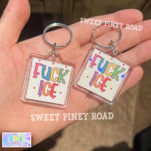 May include: Two clear acrylic keychains with silver key rings. Each keychain has a square design with the words "FUCK ICE" in colorful letters. The keychains are from "SWEET PINEY ROAD".