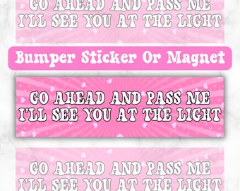 May include: Pink and white bumper sticker or magnet with the text "GO AHEAD AND PASS ME I'LL SEE YOU AT THE LIGHT" in a retro font.