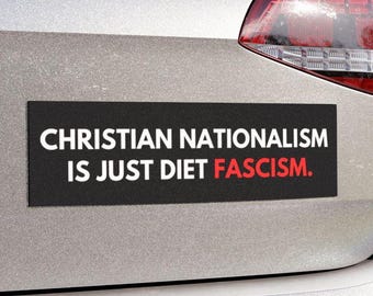 May include: A black rectangular bumper sticker with white text that reads "CHRISTIAN NATIONALISM IS JUST DIET FASCISM." The word "FASCISM" is in red. The sticker is affixed to the back of a silver car.
