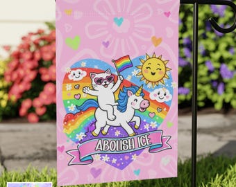 Op de afbeelding: Roze tuinvaandel met een grillig ontwerp. Een witte kat met een zonnebril rijdt op een eenhoorn over een regenboog en houdt een regenboogvlag vast. Een lachende zon en de woorden "ABOLISH ICE" zijn ook te zien. De vlag heeft de tekst "SWEET PINEY ROAD".