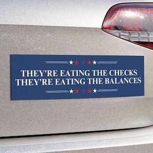 May include: A blue bumper sticker with white text that reads "They're eating the checks They're eating the balances". The sticker has five red stars and five white stars on each side of the text.