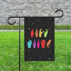 May include: A black garden flag with a rainbow design of hands signing the word "love".