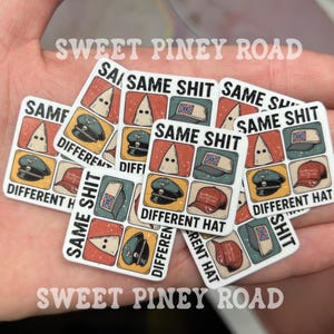 May include: A collection of square stickers with the text "SAME SHIT DIFFERENT HAT". Each sticker features a grid of images, including a KKK hood, military hats, and a Confederate flag hat. The stickers are held in a hand.
