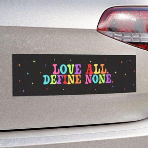 Może przedstawiać: Czarny naklejka na zderzak samochodu z tekstem "LOVE ALL. DEFINE NONE." w kolorach tęczy na czarnym tle z białymi gwiazdami.