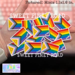 May include: A collection of Pride flag stickers, each approximately 1.1 x 1.6 inches, held in a hand. The stickers feature a rainbow design with a circle and the word "Pride". The text "SWEET PINEY ROAD" is also visible.