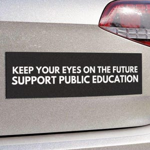 Op de afbeelding: Een zwarte bumper sticker met witte tekst die luidt: "Keep your eyes on the future. Support public education."