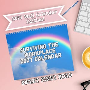 May include: A spiral-bound wall calendar titled Surviving The Workplace 2027 Calendar with a blue sky and rainbow background. A pink banner above reads 2027 Wall Calendar Edition! and the text Sweet Piney Road is printed at the bottom of the calendar.