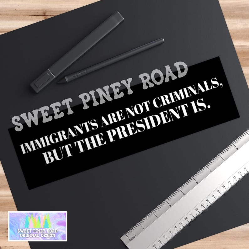 May include: A black bumper sticker with the text "SWEET PINEY ROAD IMMIGRANTS ARE NOT CRIMINALS, BUT THE PRESIDENT IS." A ruler and two black pens are also visible. The sticker has a small, colorful logo in the corner.