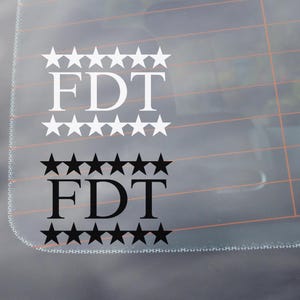 May include: Two versions of a sticker with the text "FDT" surrounded by a row of stars. The top sticker has white stars and text on a clear background. The bottom sticker has black stars and text on a clear background.