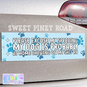 May include: A light blue car bumper sticker with the text "PLEASE EXCUSE MY SPEEDING MY DOG IS PROBABLY AT HOME CHEWING ON MY SHIT RN". The sticker has blue paw prints and stars. The brand name "SWEET PINEY ROAD" is at the top.